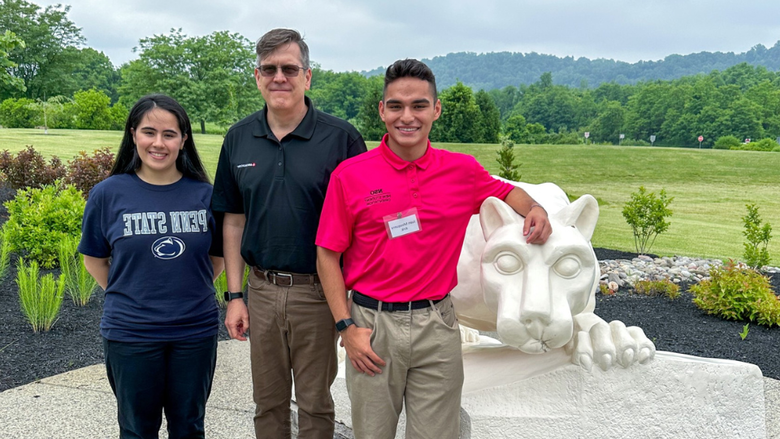 3 adults smile in front of a lion shrine 